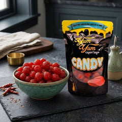 Yum Yum Candy Shop bag next to a bowl of red gummy candy on a dark surface.