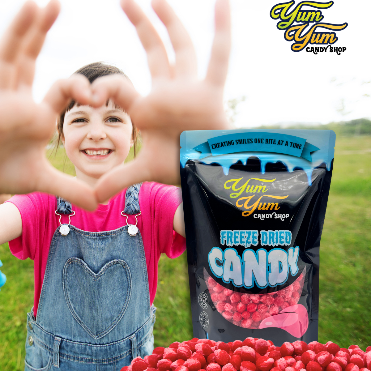 Child making a heart shape with hands, Yum Yum Candy Shop freeze-dried candy packaging, and red candy on grass.