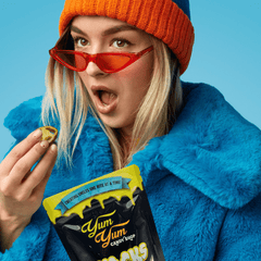 Person wearing a blue coat and orange beanie with red sunglasses, holding yum yum freeze dried jalapenos