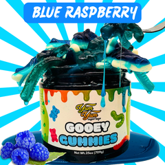 Blue Raspberry flavor Gooey Gummies jar surrounded by fresh raspberries and blue gooey candy.