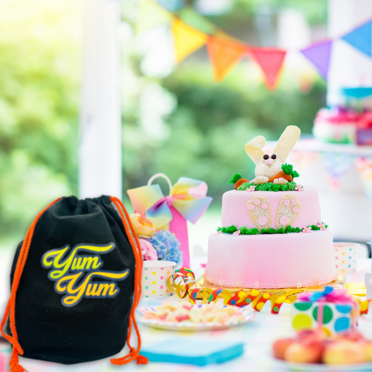 Black drawstring gift bag with orange strings next to colorful birthday cake and candy