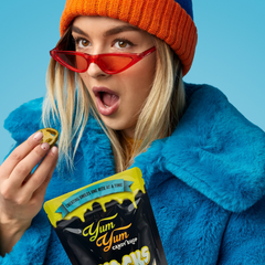 Person wearing a blue coat and orange beanie with red sunglasses, holding yum yum freeze dried jalapenos