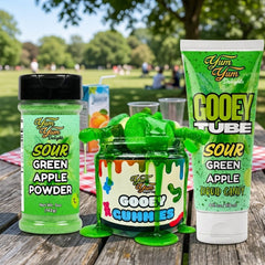 Green apple themed candy products on a wooden table with a park background