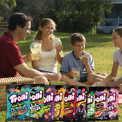 A collection of Trolli candy bags in various flavors including Strawberry Puffs, Peachy Fruit Punch, Sour Crawlers, and others displayed over a family enjoying a picnic.